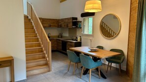 A modern kitchen with wooden cabinets, a dining table with chairs, a staircase, and pendant lighting. - REFLETS D'ARDENT 101  By Avecoeur (Montriond)