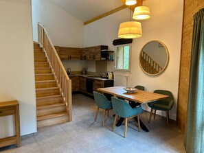 A modern kitchen with wooden cabinets, a dining table with chairs, a staircase, and pendant lighting. - REFLETS D'ARDENT 101  By Avecoeur (Montriond)