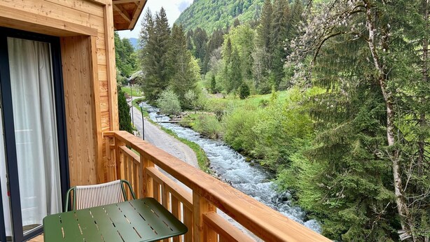 A wooden deck with a table and chairs overlooking a river and forest. - REFLETS D'ARDENT 101  By Avecoeur (Montriond)