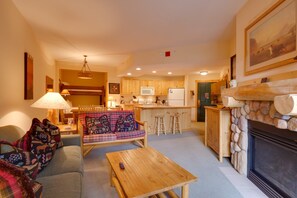 Ein gemütliches Wohnzimmer mit einer Couch, einem Couchtisch, einem Kamin und einer Küchenzeile mit Holzschränken und einer Mikrowelle.