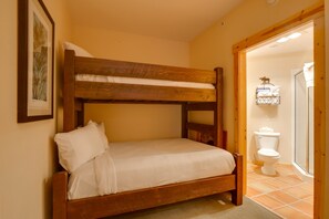 Ein Stockbett mit Holzrahmen und weißer Bettwäsche, ein gerahmtes Bild an der Wand und eine weiße Toilette mit Dusche im angrenzenden Raum.