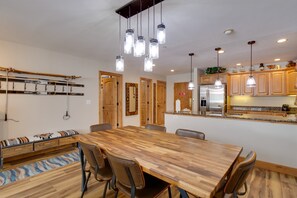 Eine moderne Küche mit Holzschränken, einer zentralen Kochinsel, hängenden Pendelleuchten und einem Essbereich mit Holztisch und Stühlen.