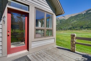 Una casa con puerta roja, ventanas amplias y vistas a un paisaje verde con montañas.