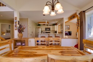 Un comedor con una mesa y sillas de madera, una cocina al fondo y una lámpara en el techo.