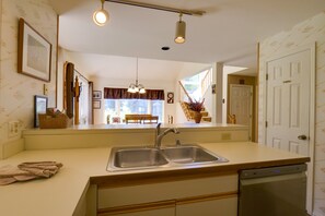 Una cocina con un lavamanos doble, lavavajillas y vista al comedor.