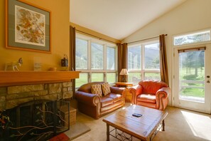 Una sala de estar con chimenea, dos sofás de cuero, una mesa de centro y ventanas grandes con vistas al verdor.