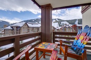 Ein Balkon mit Tisch und Stühlen, mit Blick auf einen verschneiten Berg und Gebäude.