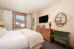 Ein Hotelzimmer mit Bett, Schminktisch, Fernseher, Spiegel und Fenster mit Blick auf Bäume und Schnee.