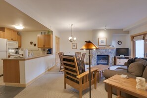 Eine moderne Küche mit Holzausstattung, eine Essecke mit Tisch und Stühlen, ein Kamin und ein Wohnzimmer mit einer Couch.
