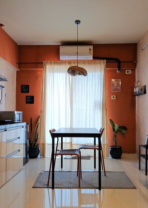 Een moderne keuken met een eettafel, stoelen, een hanglamp en een potplant.