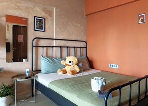 Een slaapkamer met een bed, een nachtkastje, een teddybeer, een spiegel en een aan de muur hangend schilderij.
