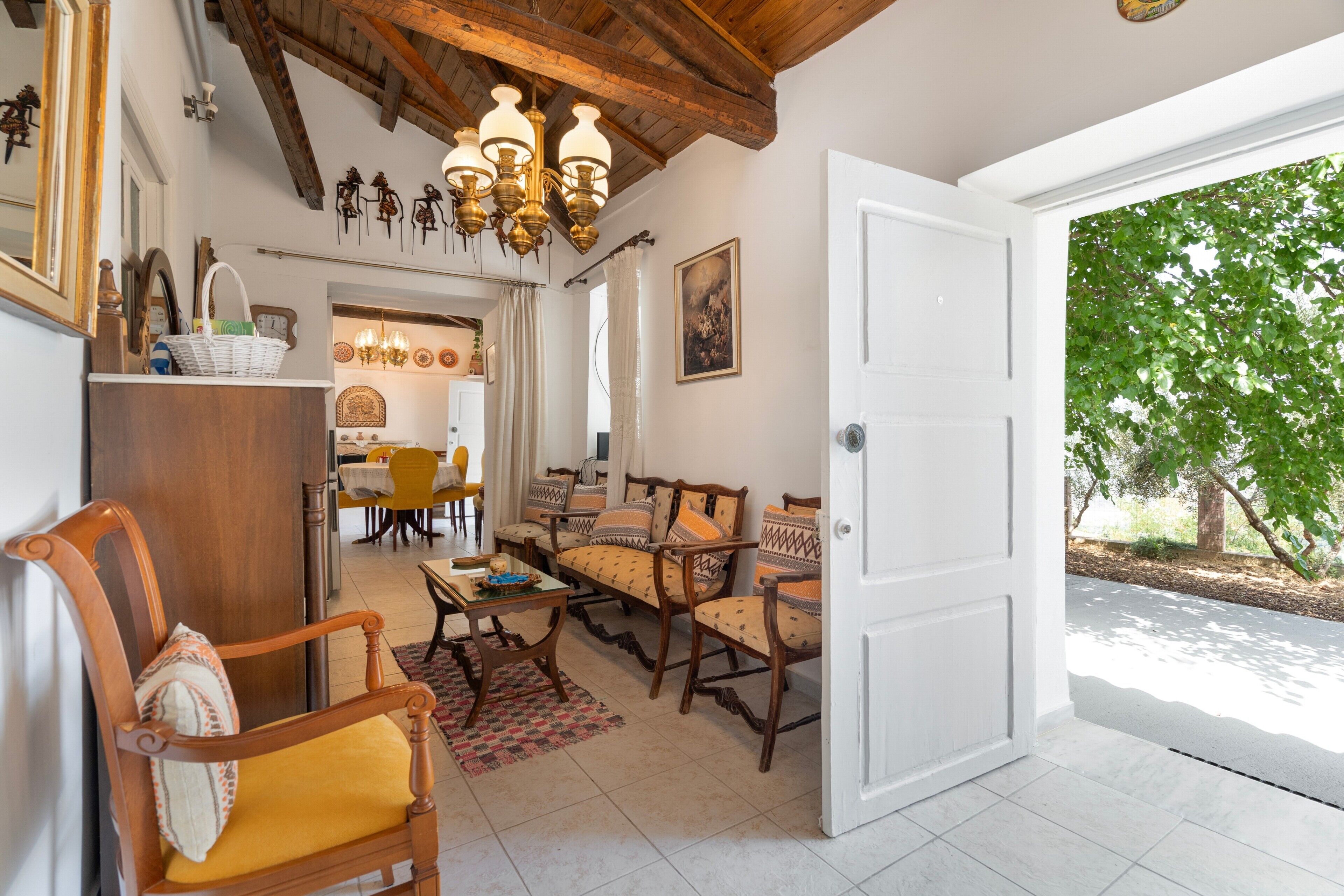 A room with a dining area, a seating area with patterned cushions, and a large open door leading outside.