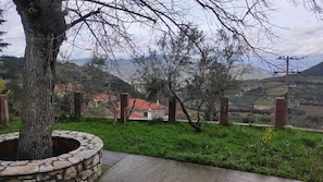 Eine Steinsitzbank mit Baum, einer Rasenfläche und weiter Aussicht auf Häuser und Hügel.