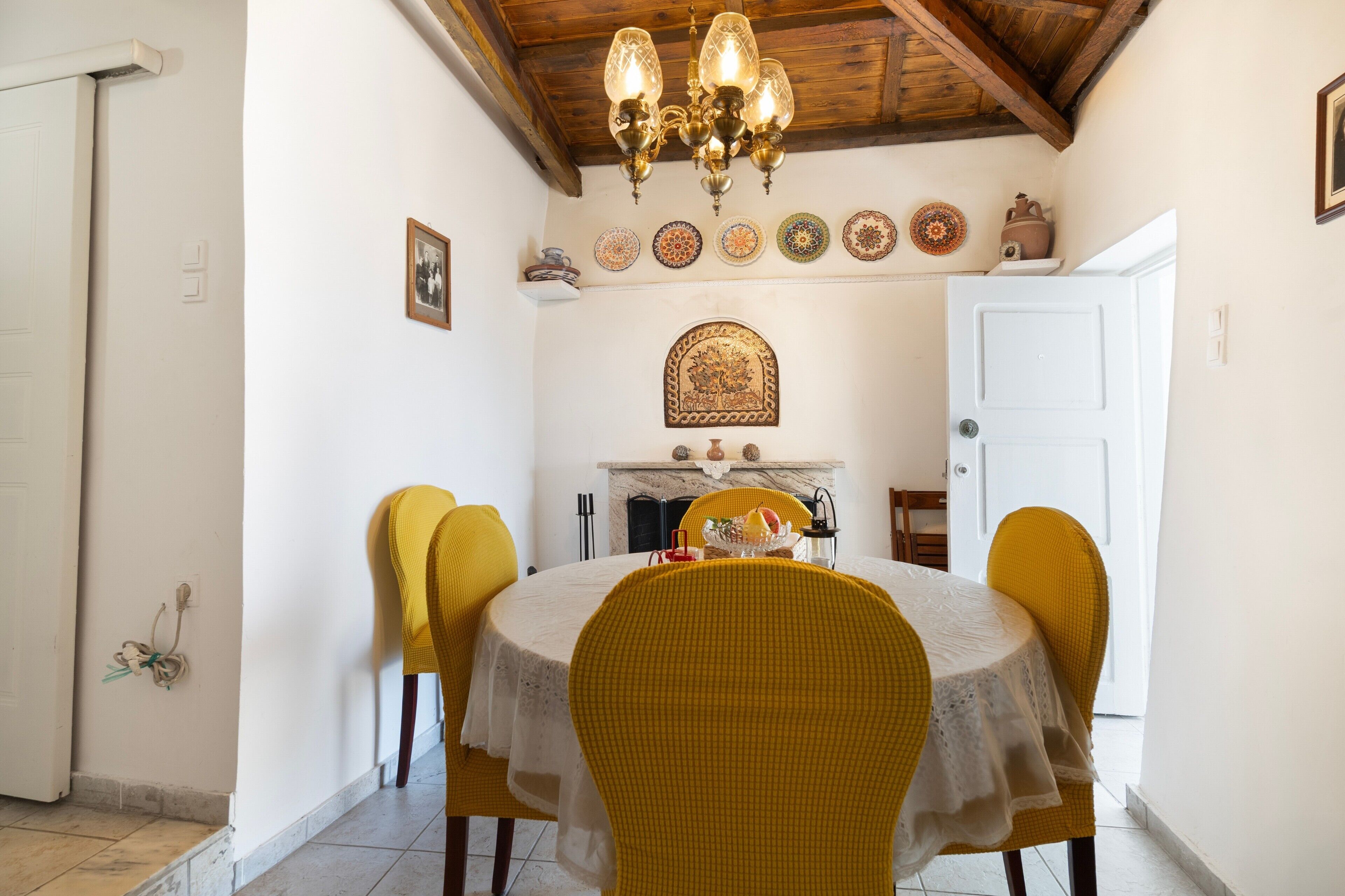 Un comedor con una mesa redonda, sillas amarillas, una araña y una chimenea.