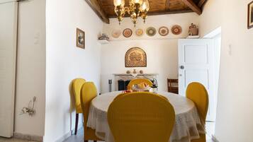 Un comedor con una mesa redonda, sillas amarillas, una araña y una chimenea.