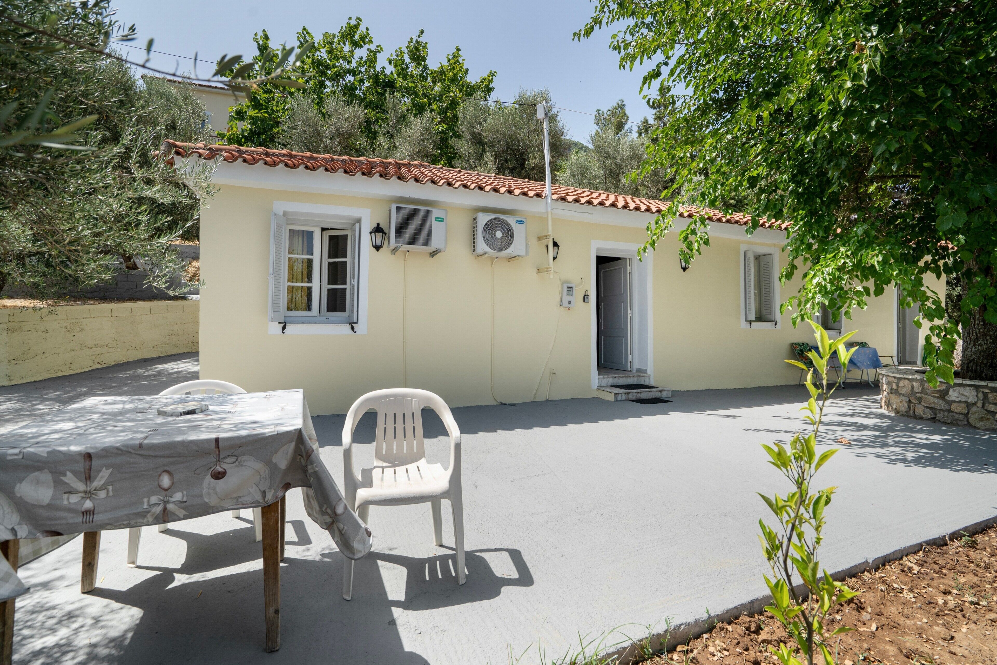 A building with a tiled roof, air conditioning units, a door, and a table with a chair.