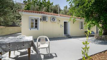 A building with a tiled roof, air conditioning units, a door, and a table with a chair.