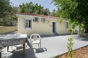 A building with a tiled roof, air conditioning units, a door, and a table with a chair. - Giannis Mountain House — Mountain Tranquility with View & Private Garden, Near Aigio (Mageiras)