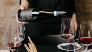A person pouring wine into glasses on a table with a stone wall background. - Villa del Brolo - Famiglia Furia (Mezzane di Sotto)