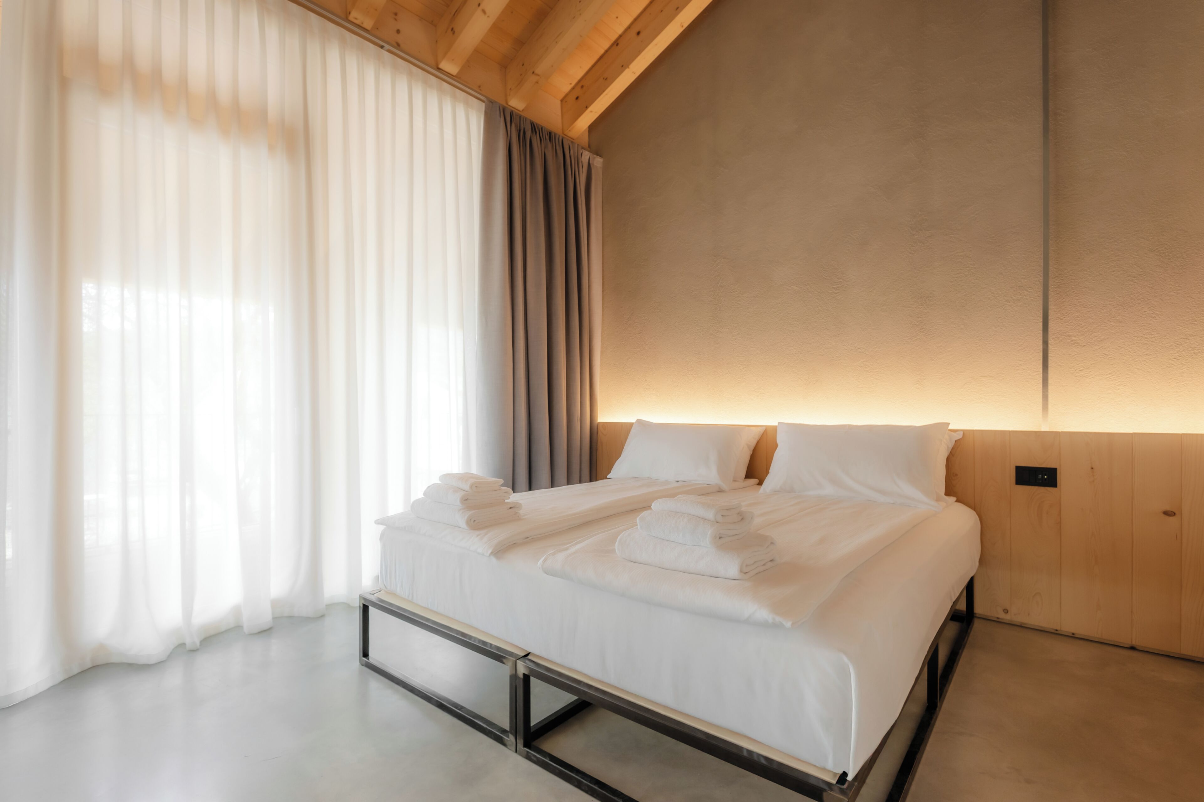 A modern hotel room with a bed, curtains, and a wooden ceiling.