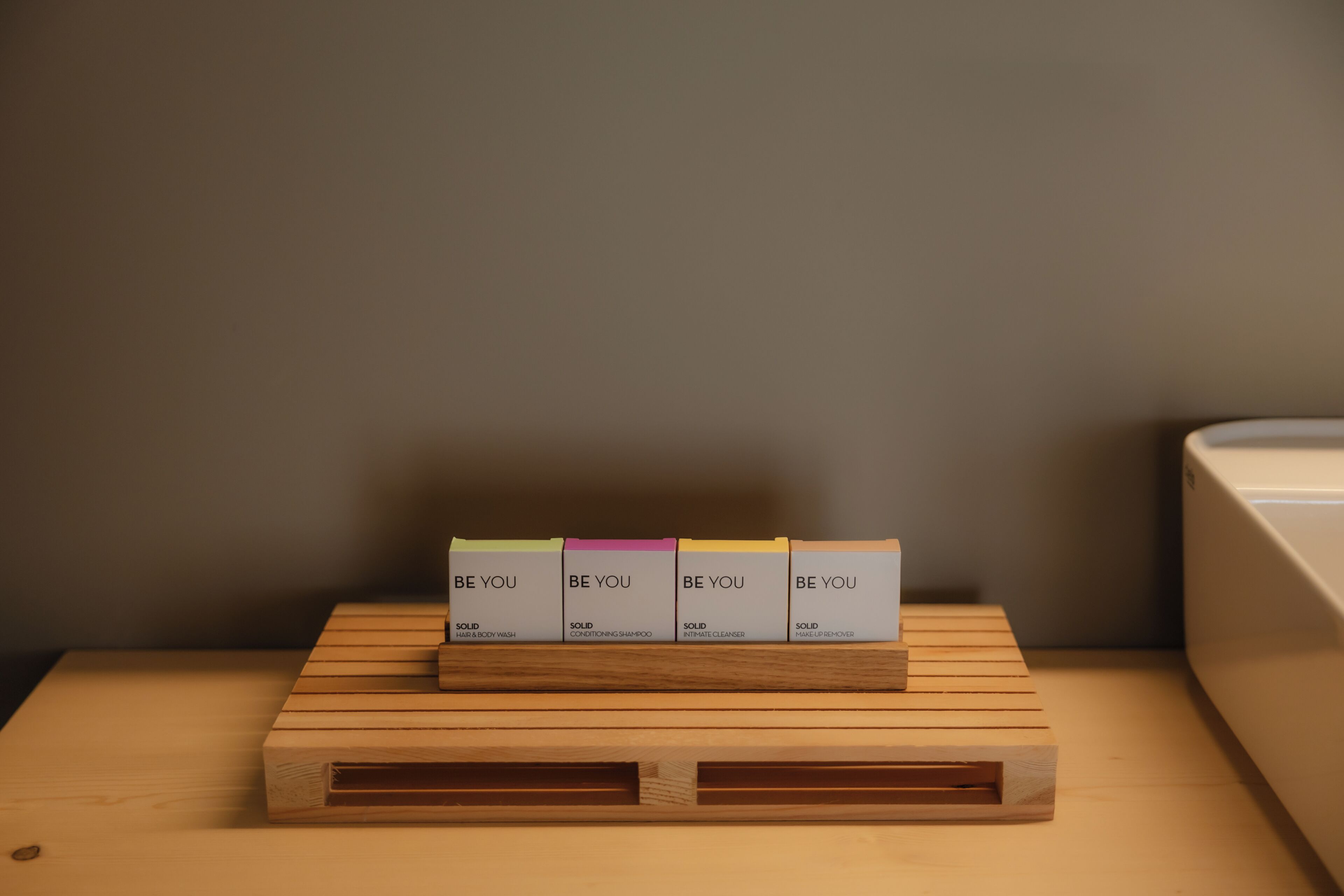 Un expositor de madera con cuatro cajas etiquetadas 'BE YOU' y 'SOLID', con diferentes nombres de productos.