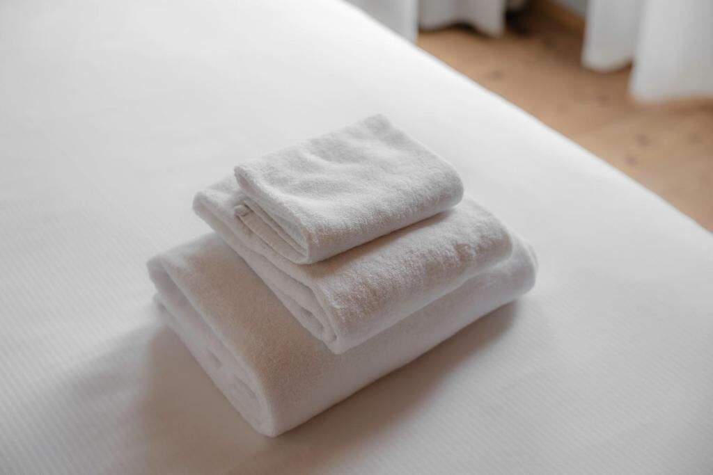 Toalha branca dobrada sobre uma cama branca em um quarto com piso de madeira.