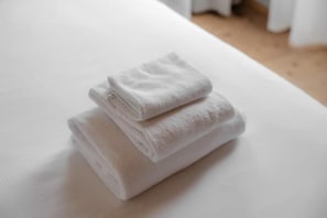 A neatly folded white towel on a white bed in a room with a wooden floor.