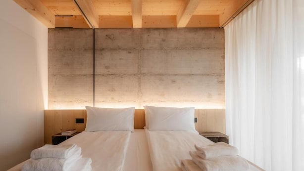 A double bed with white linens and towels, a concrete headboard, and a bedside table with a lamp. - Villa del Brolo - Famiglia Furia (Mezzane di Sotto)