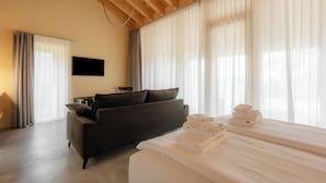 A hotel room with a bed, a sofa, a flat-screen TV, and large windows with curtains. - Villa del Brolo - Famiglia Furia (Mezzane di Sotto)