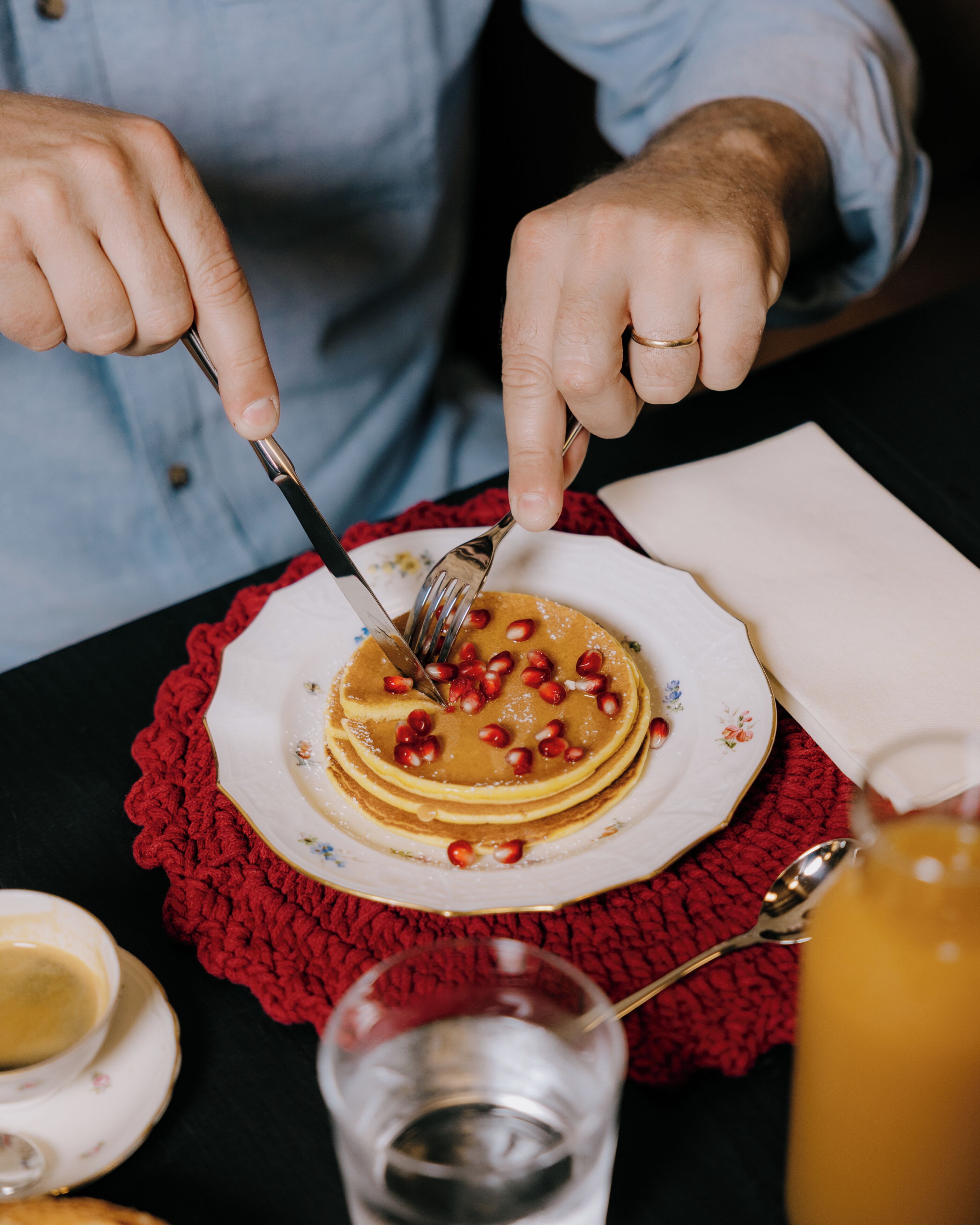 A person cutting a stack of pancakes with a fork and knife on a plate with a red doily.