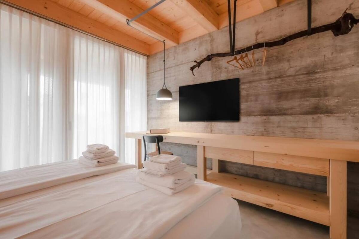 Ein modernes Zimmer mit einem Bett, einem Holztisch, einem Fernseher und einem Fenster mit Vorhängen.