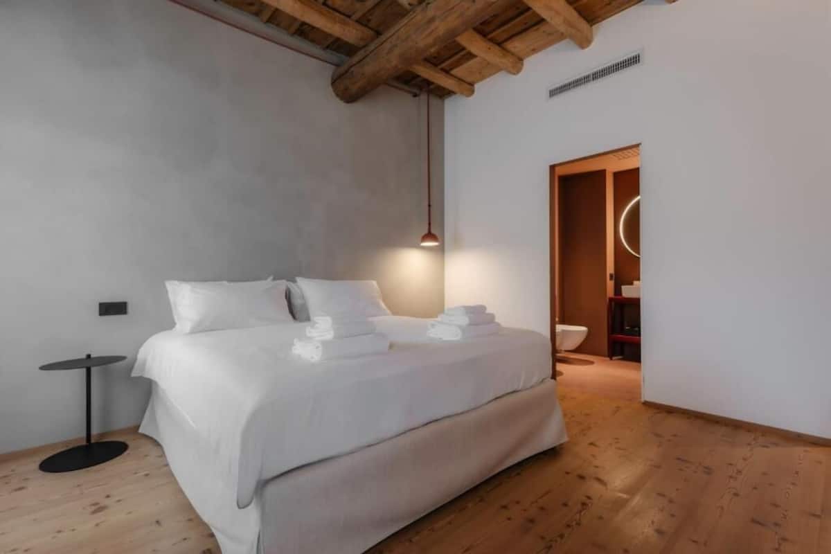 A modern bedroom with a large bed, a small round table, and a wooden ceiling.
