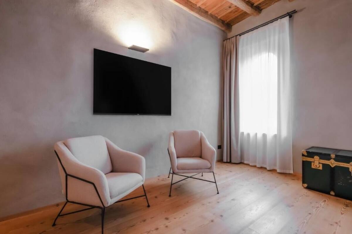 Ein Zimmer mit einem wandmontierten Flachbildfernseher, zwei Sesseln, Holzboden und einem Vorhangfenster.