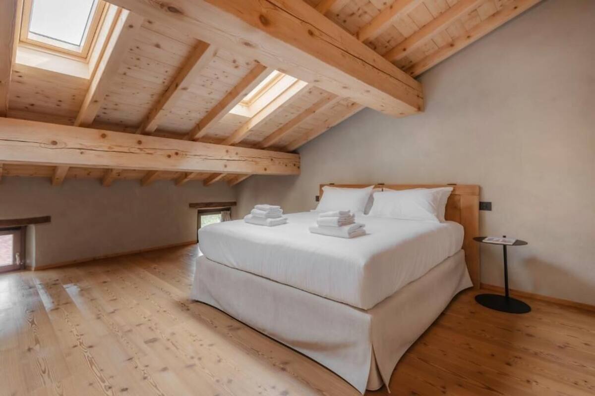 Ein Schlafzimmer mit Holzbalkendecke, einem Bett mit weißer Bettwäsche und einem kleinen Nachttisch.