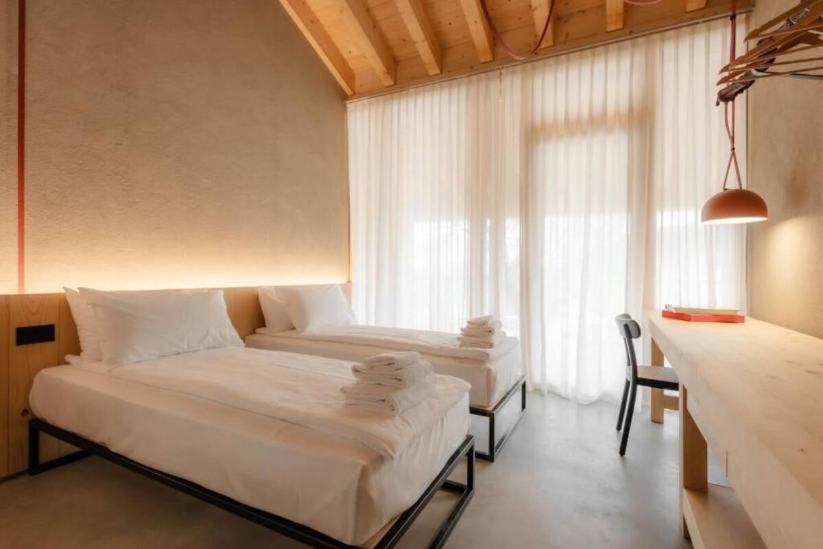 Ein Hotelzimmer mit zwei Betten, einer Holzbalkendecke, einem Schreibtisch und einem Stuhl.
