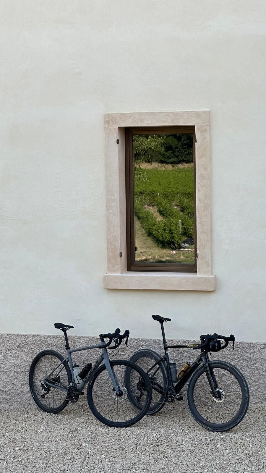 A window with a view of a green landscape, three bicycles parked in front, and a textured wall.