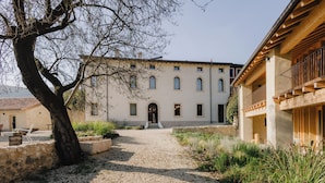 A building with a gravel path leading to a door, surrounded by greenery and a tree. - Villa del Brolo - Famiglia Furia (Mezzane di Sotto)