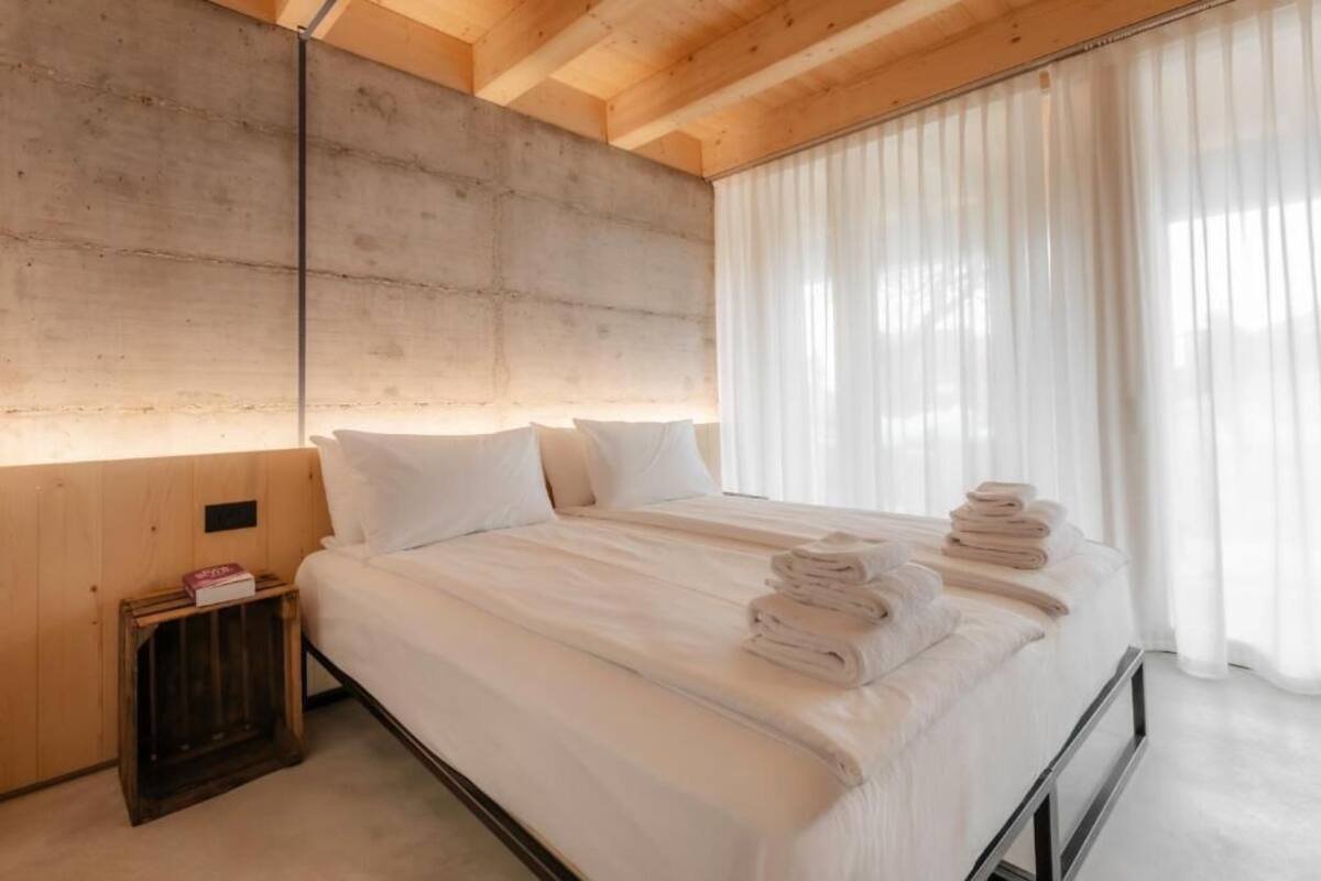 Ein Schlafzimmer mit Bett, Kissen, einem Holzkopfteil, einem Nachttisch und einem Fenster mit Vorhängen.