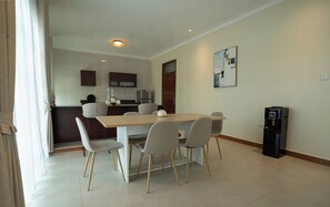 Uma área de refeições com mesa e cadeiras, uma cozinha ao fundo e um bebedouro.