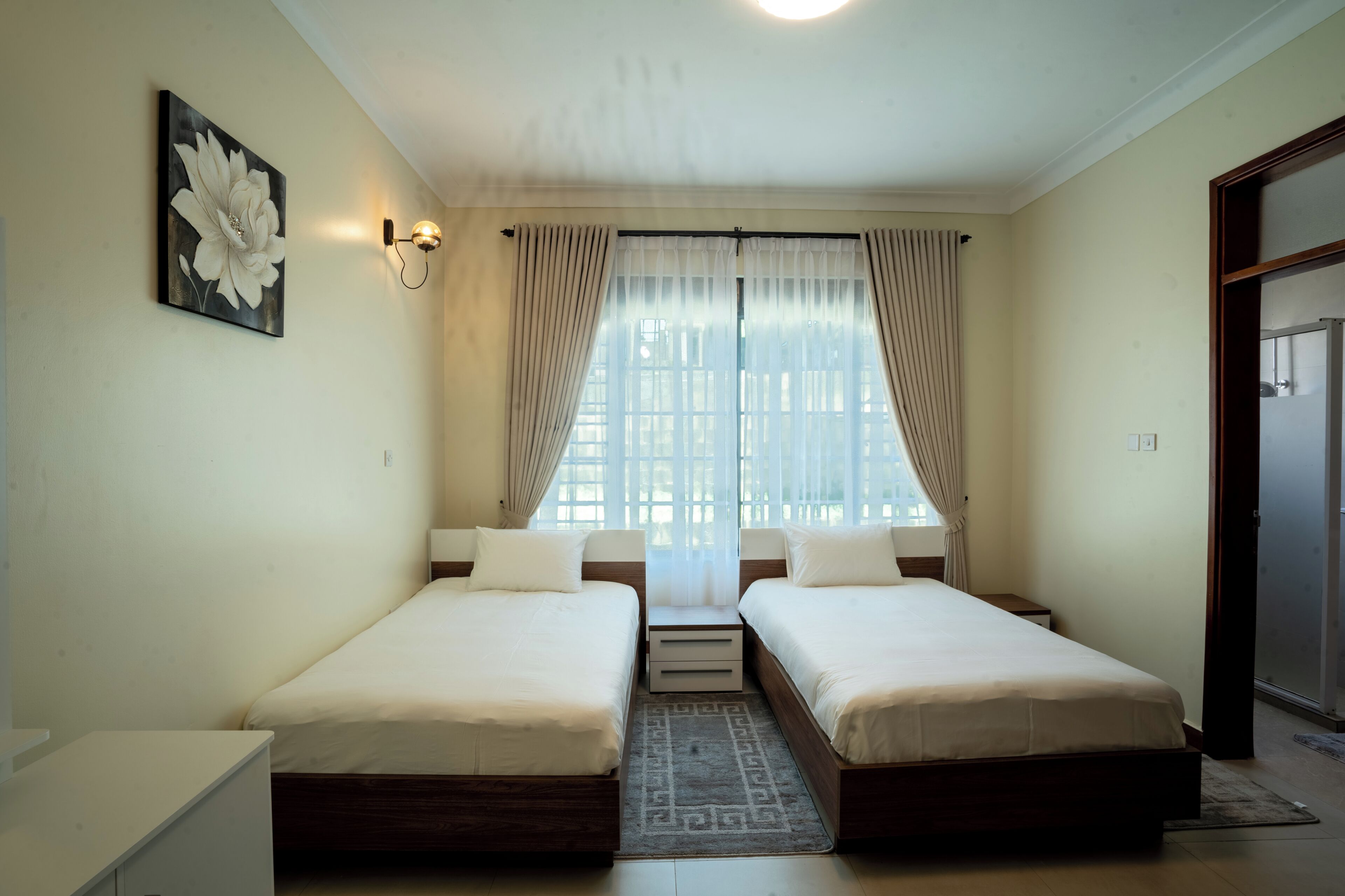 Un dormitorio con dos camas, una ventana con cortinas, una lámpara de pared y una puerta.