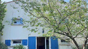 Un bâtiment à la façade blanche, aux volets bleus, avec un arbre devant.