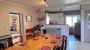 Une salle à manger avec une table en bois dressée pour six personnes, des meubles de cuisine, un réfrigérateur et un piano placé dans un coin.