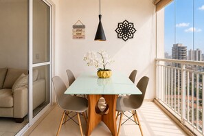 A balcony with a dining area, a sofa, a hanging light, and decorative wall art.