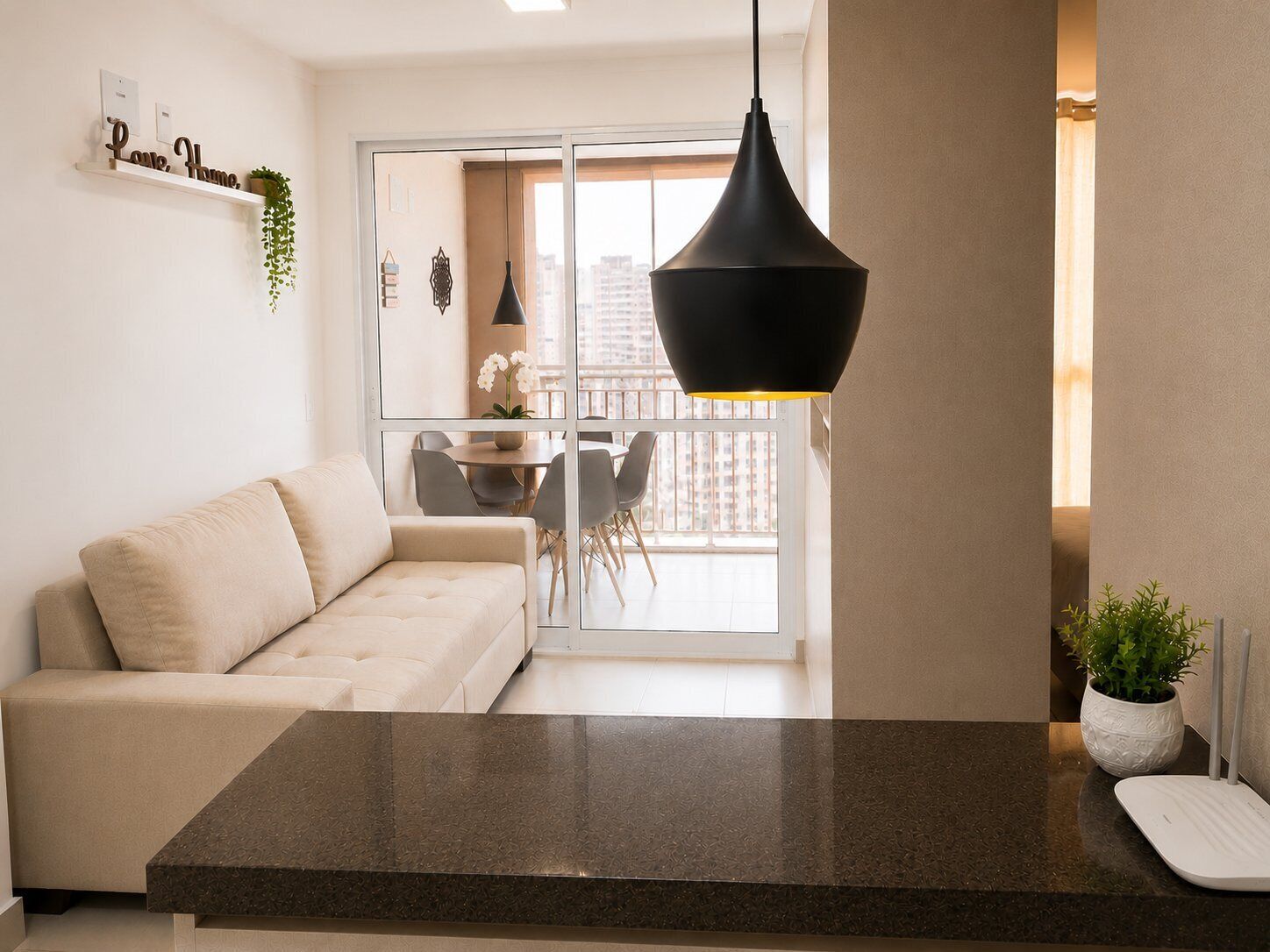 Uma sala de estar moderna com sofá, mesa de jantar com cadeiras, luminária pendente preta e vista da cidade através de grandes janelas.
