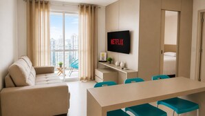 A modern hotel room with a sofa, a dining table with chairs, a TV, and a balcony with curtains. - Walk Bueno (Goiânia)