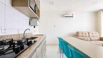 Una cocina moderna con estufa a gas, armarios blancos y una zona de comedor con sofá y sillas.