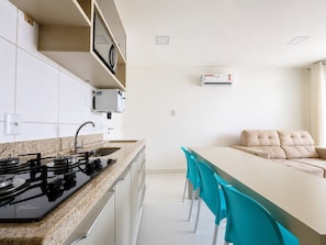 Una cocina moderna con estufa a gas, armarios blancos y una zona de comedor con sofá y sillas.