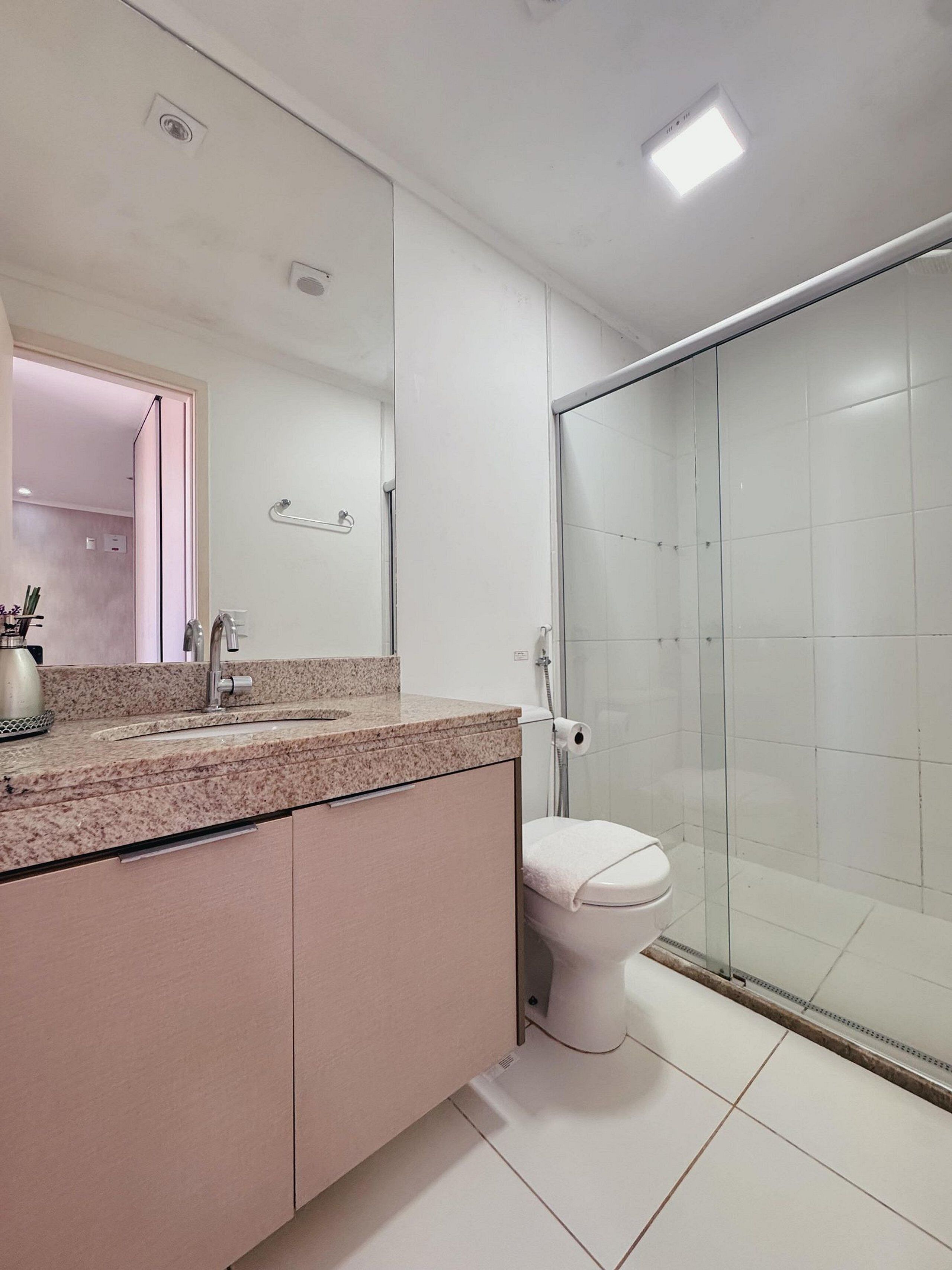 Um banheiro moderno com bancada de granito, vaso sanitário e box de vidro.