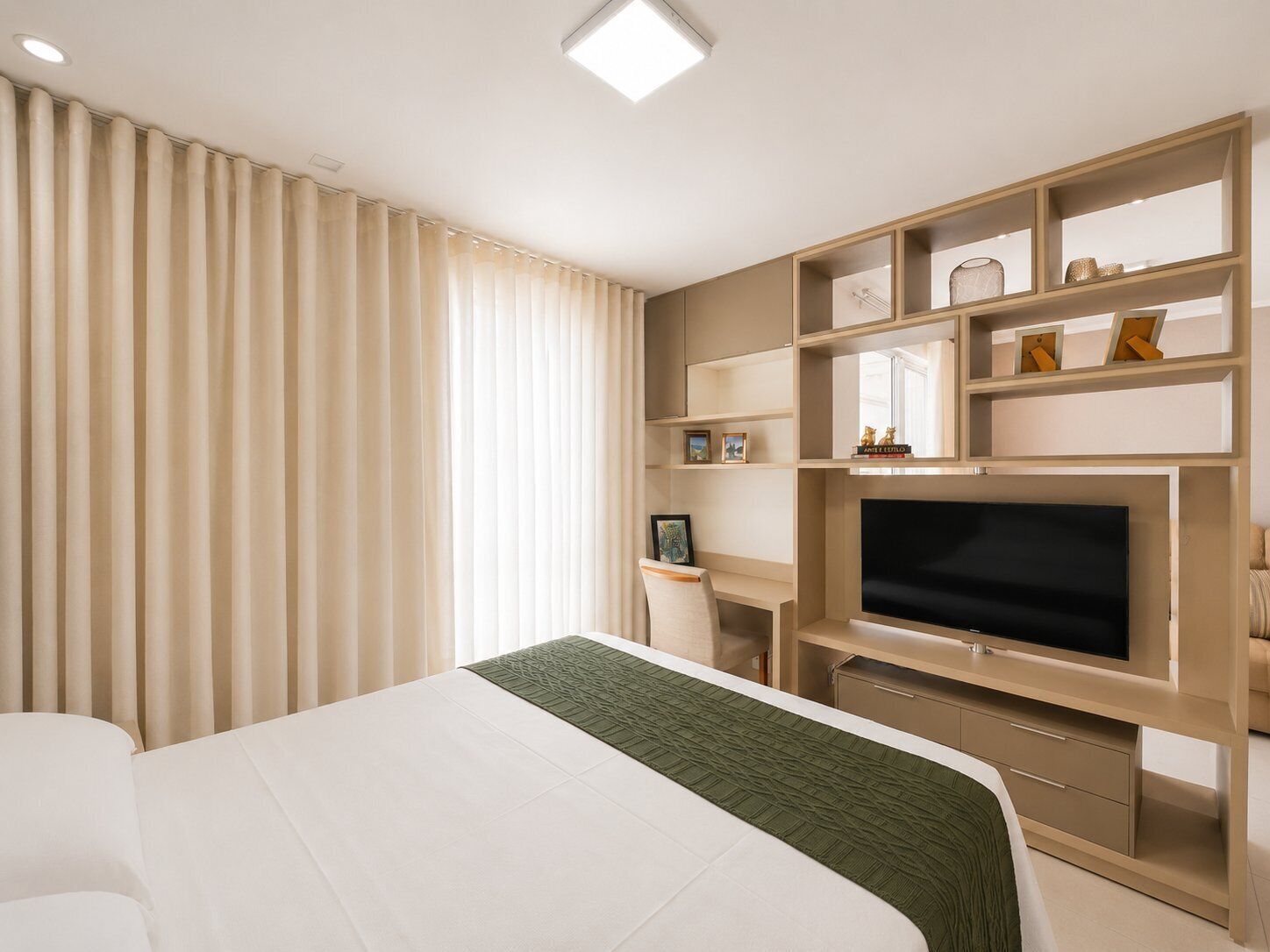 A hotel room with a bed, a TV, and built-in shelves with decorative items.