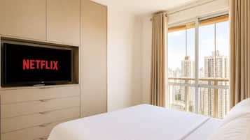 Una habitación de hotel con cama, televisor montado en la pared y ventana con cortinas.